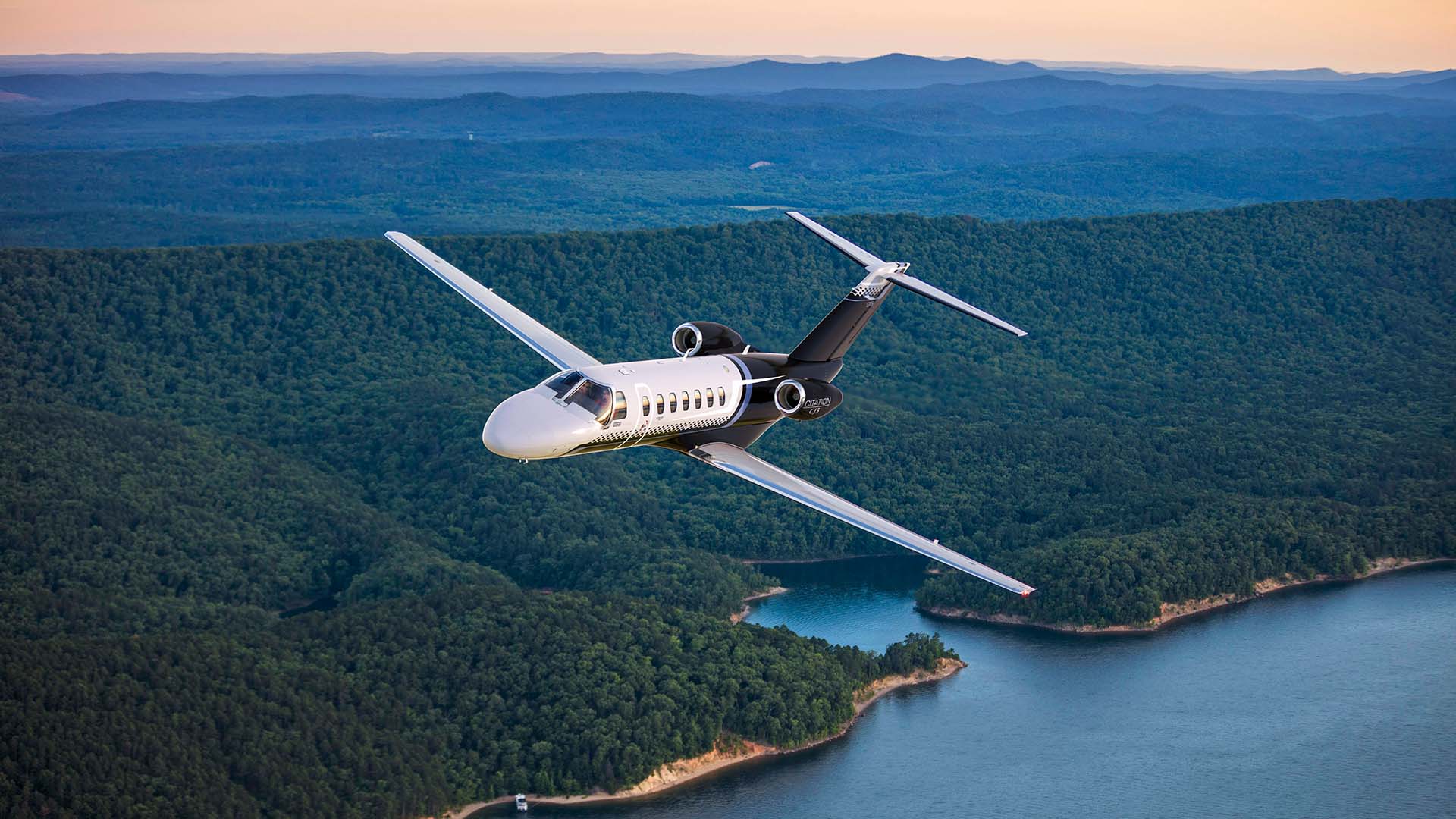 Prywatny odrzutowiec Citation CJ3 w locie nad lasem i jeziorem o zachodzie słońca